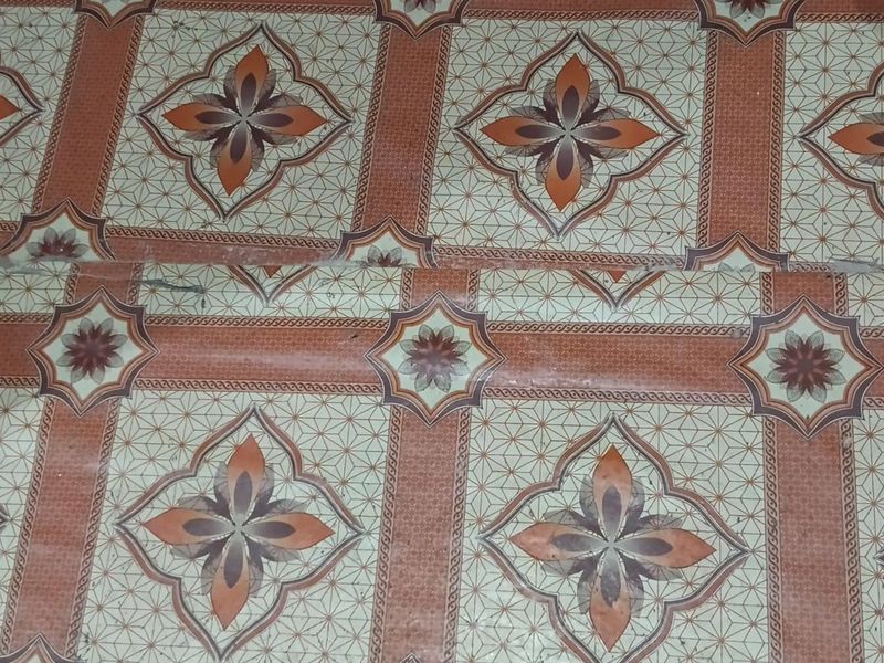 Close-up view of dated patterned vinyl flooring showing visible seams and signs of wear.