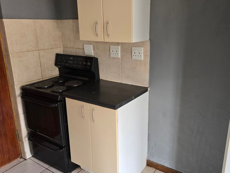 A compact kitchen area featuring basic built-in cabinetry, a tiled splashback, and a freestanding stove, offering a functional space ready for modernization.
