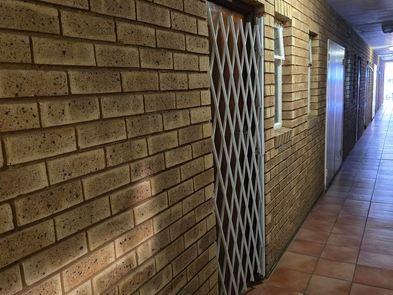 A long apartment hallway featuring exposed brick walls, tiled flooring, and secure metal gates at the unit entrances.