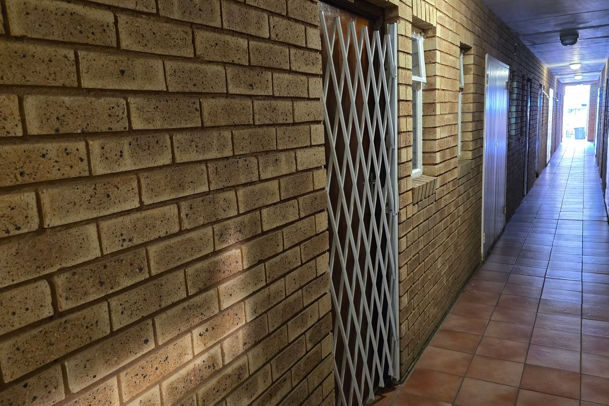 A long apartment hallway featuring exposed brick walls, tiled flooring, and secure metal gates at the unit entrances.
