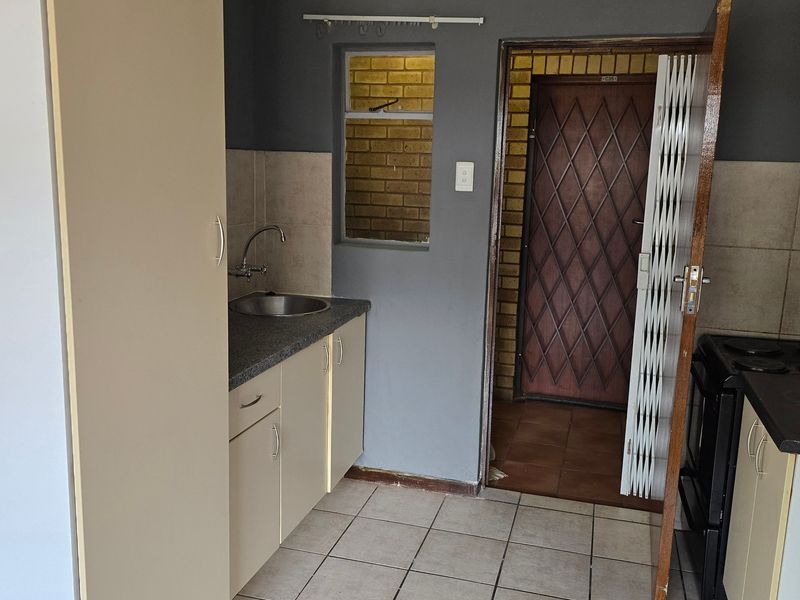 A compact kitchen featuring built-in cabinetry, a stainless steel sink, tiled flooring, and an electric stove, with direct access to an external security gate.
