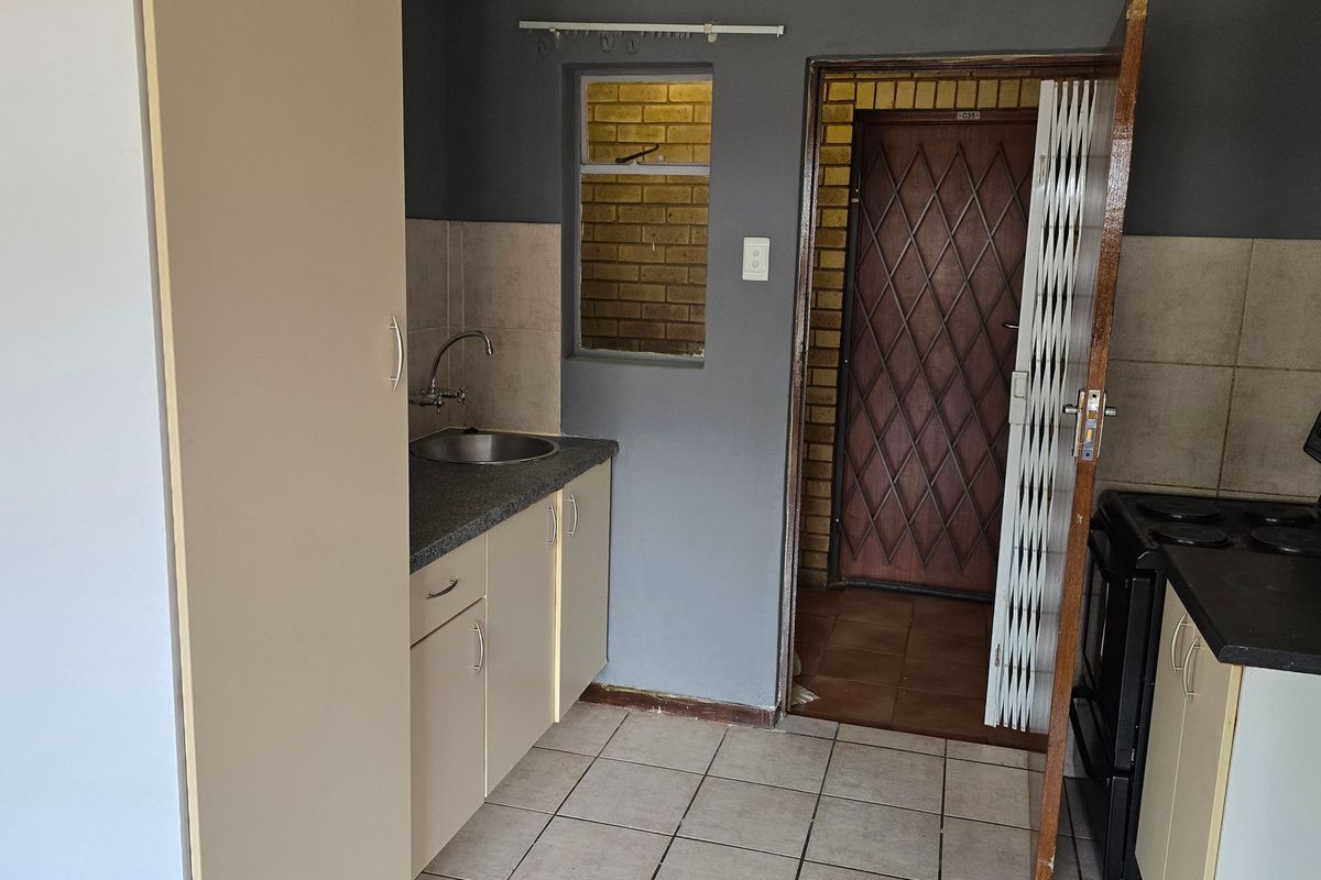 A compact kitchen featuring built-in cabinetry, a stainless steel sink, tiled flooring, and an electric stove, with direct access to an external security gate.