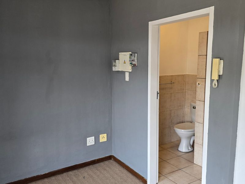 A view into a small bathroom featuring a toilet and tiled finishes, adjacent to a living area with an intercom and electrical distribution board.