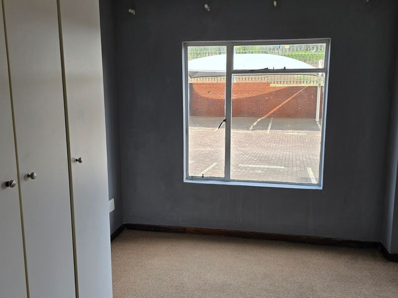 A vacant bedroom featuring built-in cupboards, carpeted flooring, and large windows overlooking the parking area.