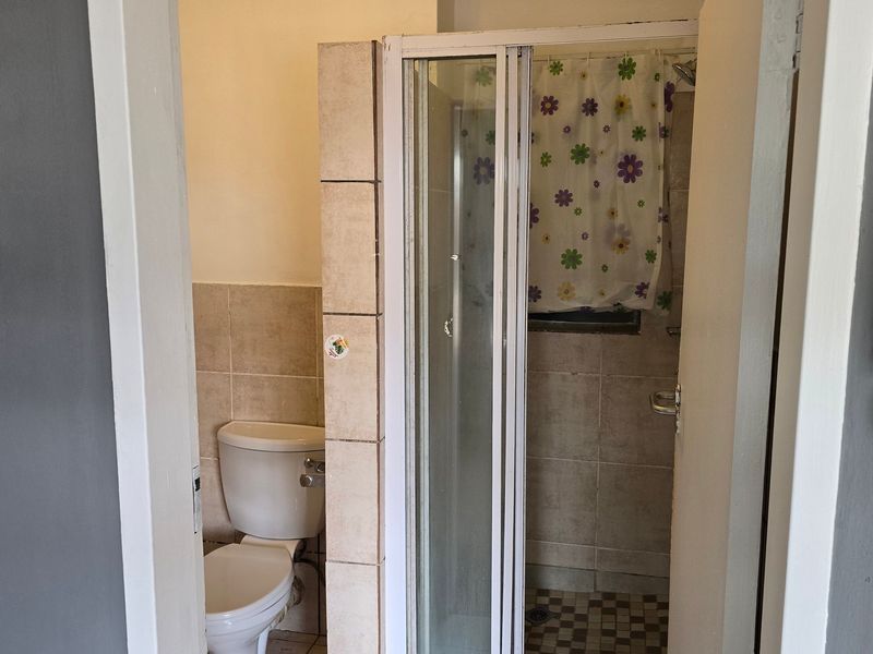 A functional bathroom featuring a separate toilet and shower enclosure with tiled finishes, requiring cosmetic updates to modernize the space.