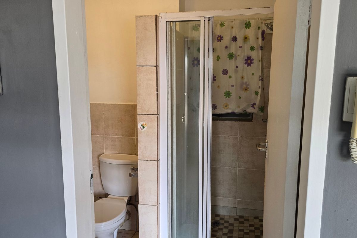 A functional bathroom featuring a separate toilet and shower enclosure with tiled finishes, requiring cosmetic updates to modernize the space.