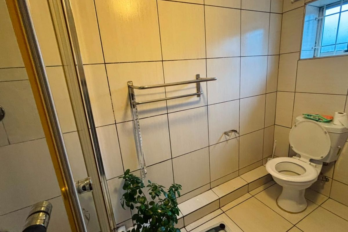 A functional bathroom featuring a shower enclosure, tiled walls and flooring, and a standard toilet, with a window providing natural light.