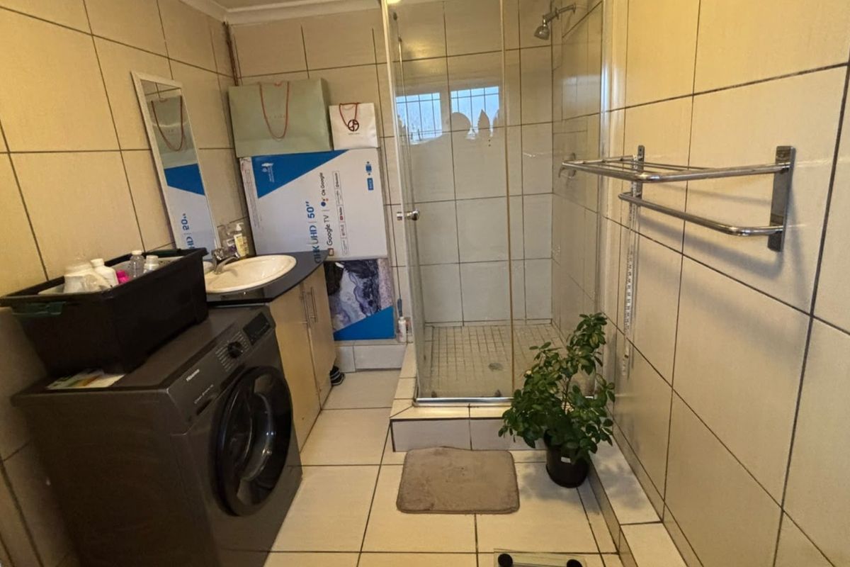 A functional bathroom featuring a shower enclosure, vanity cabinet with basin, and full-height wall tiling.