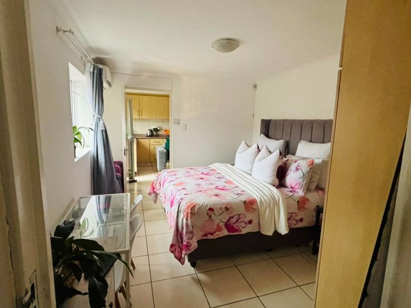 A bedroom featuring tiled flooring and an air conditioning unit, with a view through to the adjacent kitchen area.