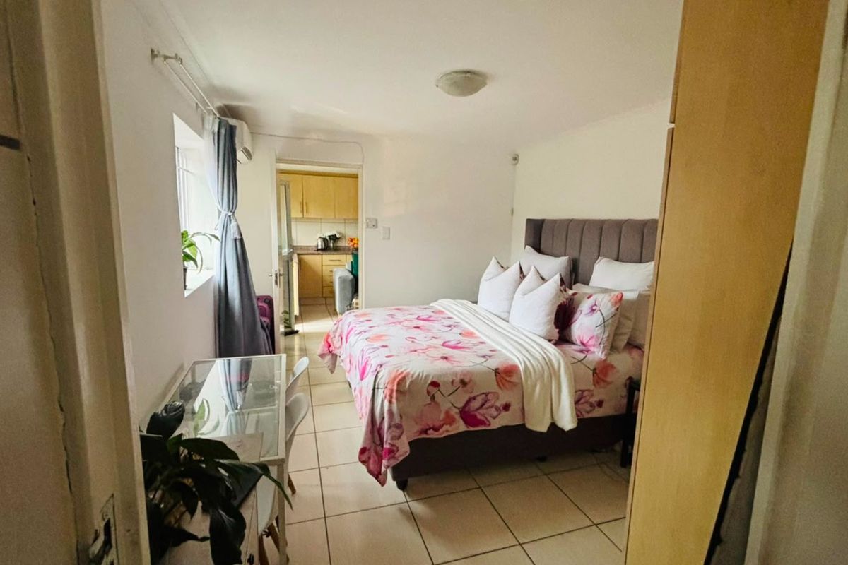 A bedroom featuring tiled flooring and an air conditioning unit, with a view through to the adjacent kitchen area.