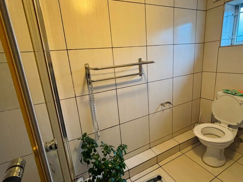 A functional bathroom featuring a shower enclosure, tiled walls and flooring, and a standard toilet, with a window providing natural light.