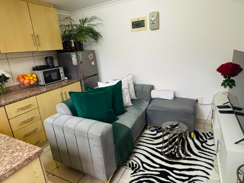 Compact open-plan living area featuring a functional kitchen with laminate cabinetry and tiled flooring, seamlessly integrated with the lounge space.