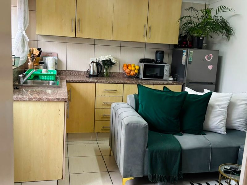 Compact open-plan kitchen featuring light wood-tone cabinetry, granite countertops, and tiled flooring, seamlessly integrated with the adjacent living area.