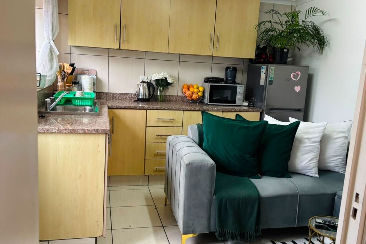Compact open-plan kitchen featuring light wood-tone cabinetry, granite countertops, and tiled flooring, seamlessly integrated with the adjacent living area.
