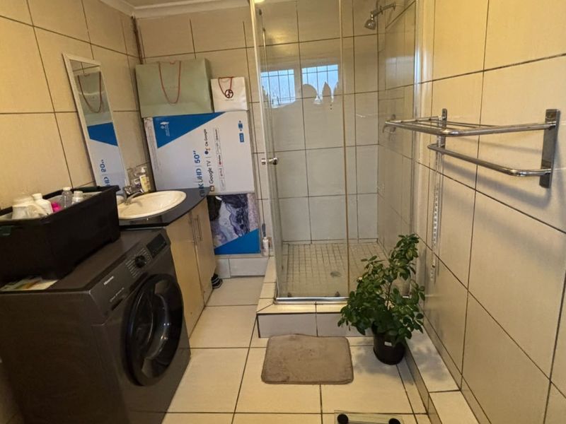 A functional bathroom featuring a shower enclosure, vanity cabinet with basin, and full-height wall tiling.