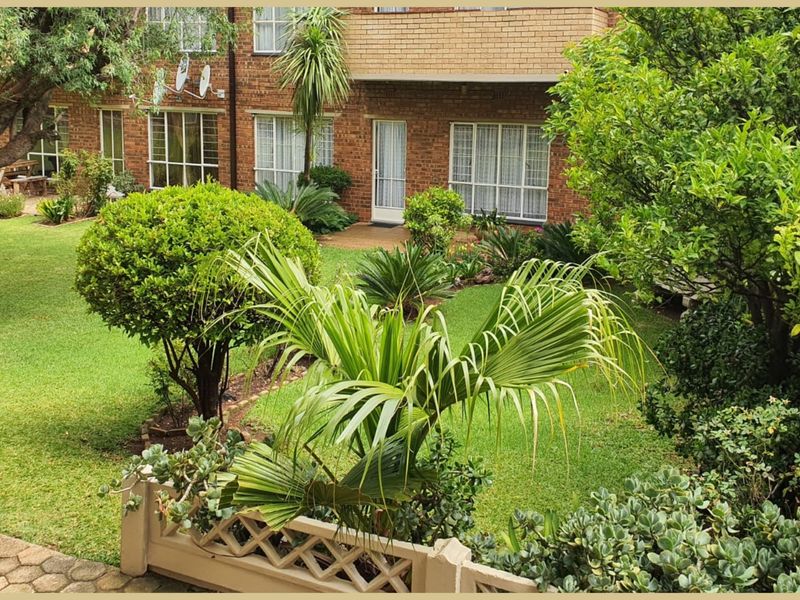 A view of the rear brick facade of the flat, featuring a well-maintained garden and a paved patio area.