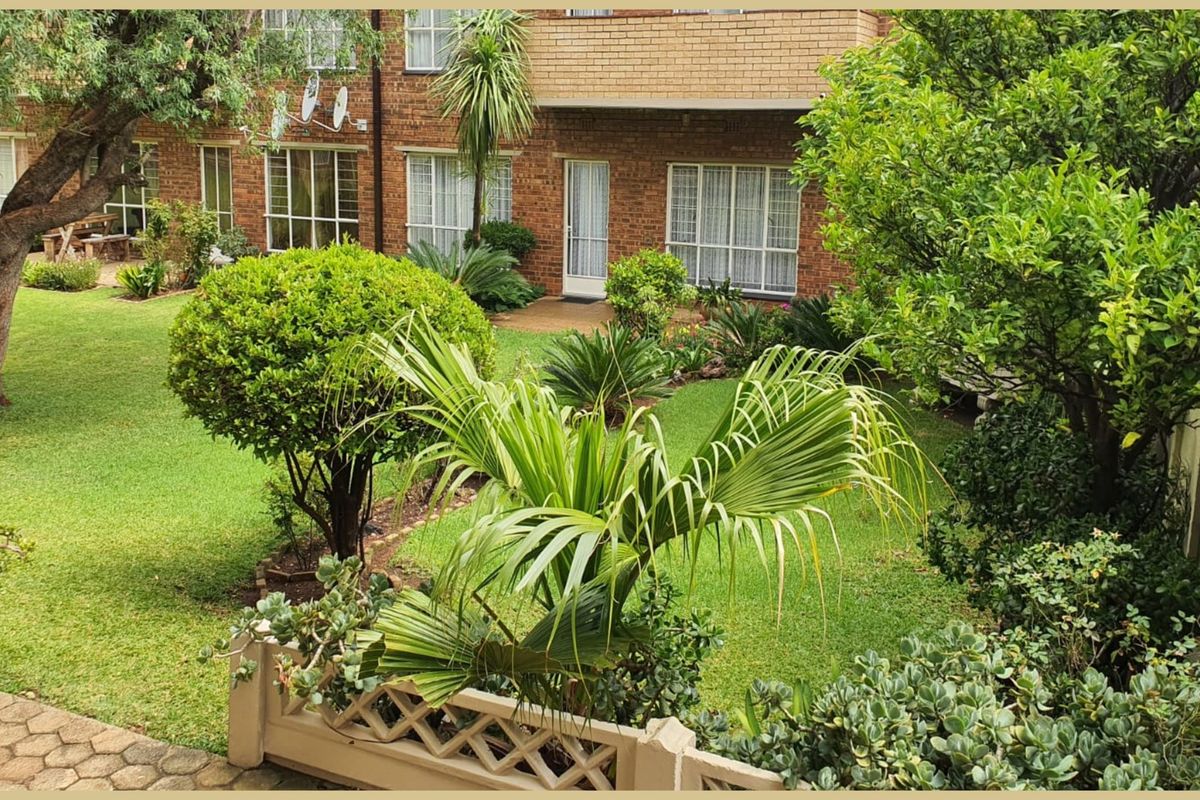 A view of the rear brick facade of the flat, featuring a well-maintained garden and a paved patio area.