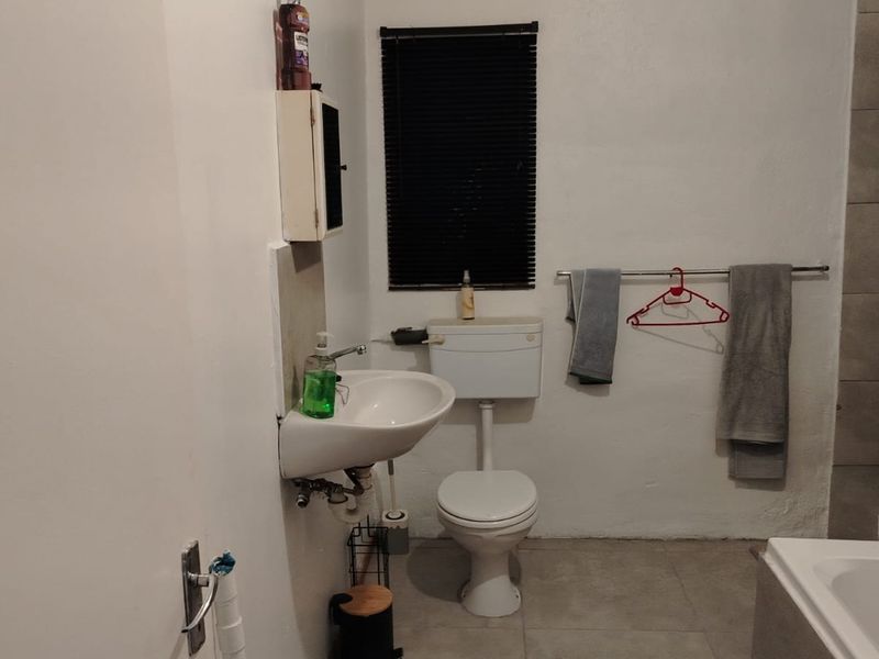 A functional bathroom featuring a wall-mounted basin, toilet, bathtub, and tiled shower area with neutral finishes.