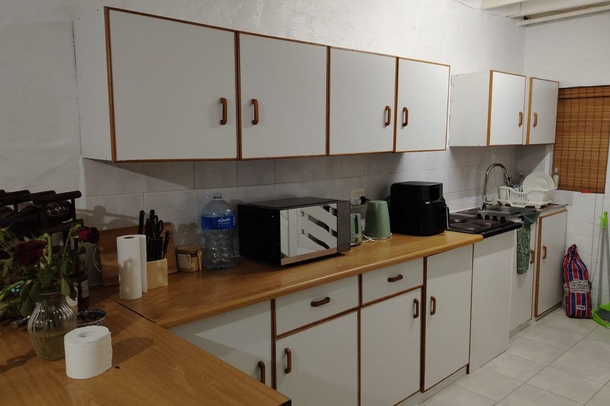 A functional kitchen featuring white cabinetry with wood trim, laminate countertops, tiled backsplash, and a stainless steel sink.