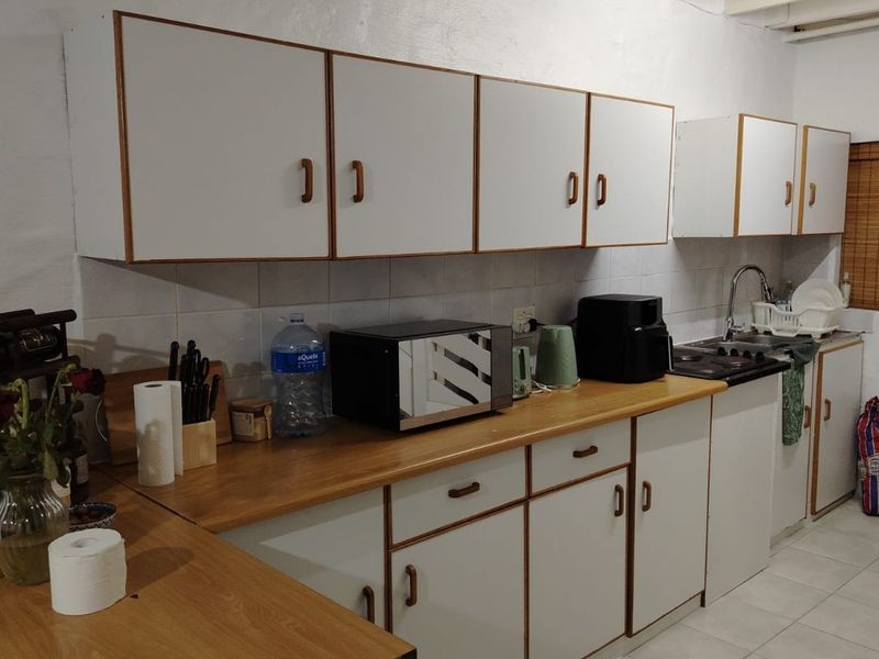 A functional kitchen featuring white cabinetry with wood trim, laminate countertops, tiled backsplash, and a stainless steel sink.