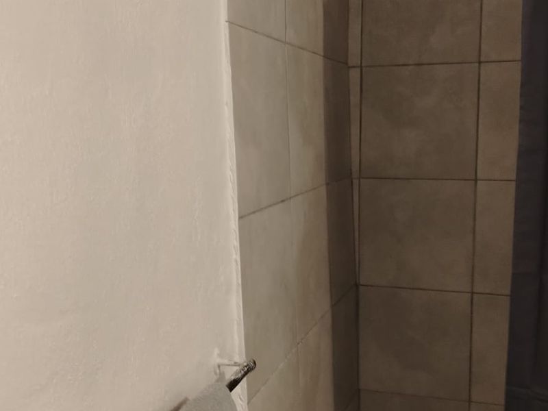 A close-up view of a bathroom shower area featuring neutral-toned wall tiles.