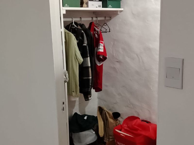 A small utility or storage closet featuring built-in shelving and a hanging rail for organized storage.