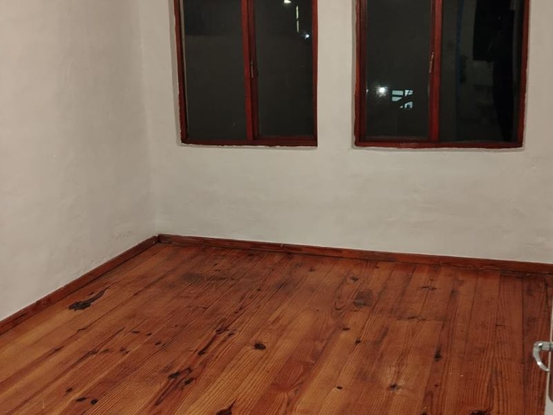 An empty bedroom featuring original timber flooring and wooden window frames, offering a blank canvas for personalization.