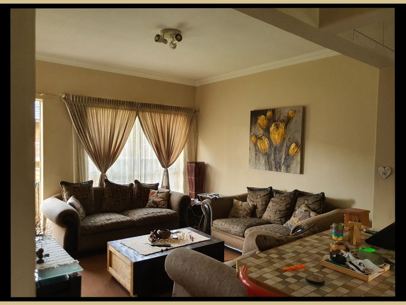 A comfortable living room area featuring neutral wall tones, ceiling cornice detailing, and natural light through window treatments.