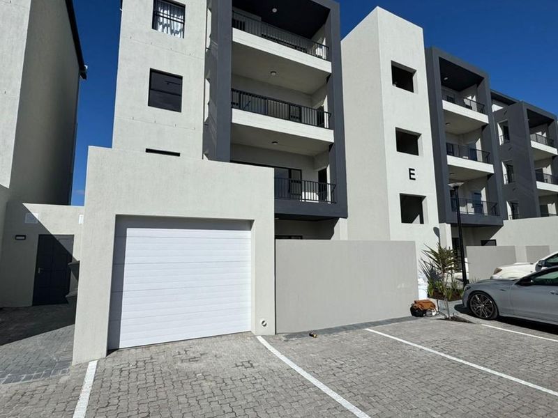 Modern apartment complex exterior featuring a private garage, paved parking area, and multi-level balconies with contemporary architectural design.