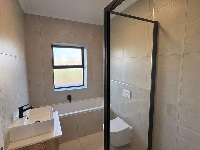 Modern bathroom featuring a built-in bathtub, wall-mounted toilet, shower enclosure, and contemporary vanity with black fixtures and neutral wall tiling.