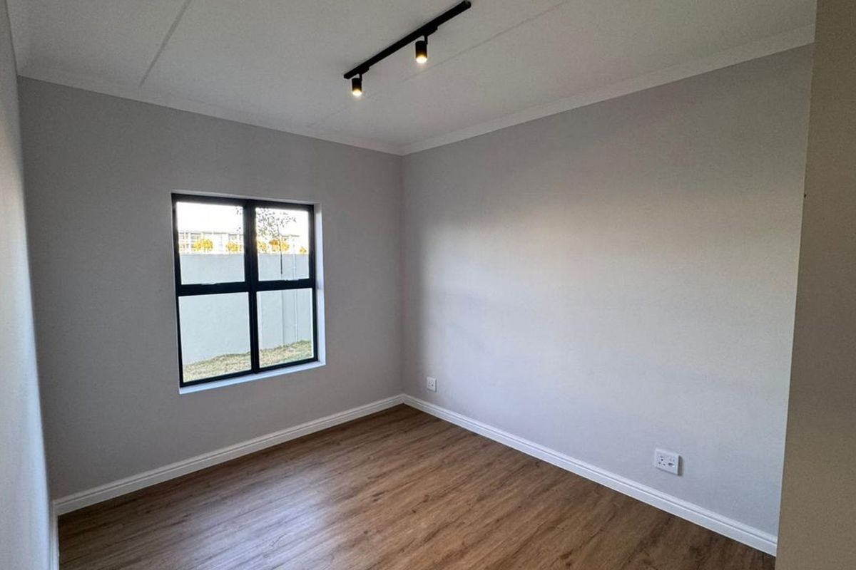 A clean, empty bedroom featuring modern laminate flooring, neutral walls, and contemporary track lighting, ready for personalization.