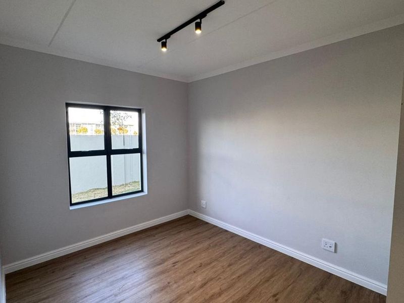 A clean, empty bedroom featuring modern laminate flooring, neutral walls, and contemporary track lighting, ready for personalization.