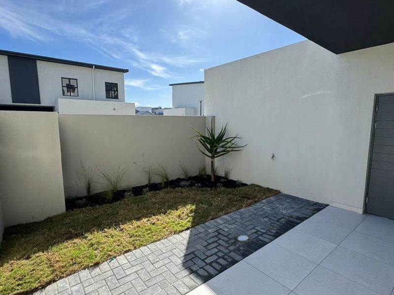 A private rear courtyard featuring a paved patio area, a small landscaped garden bed, and a secure external door.