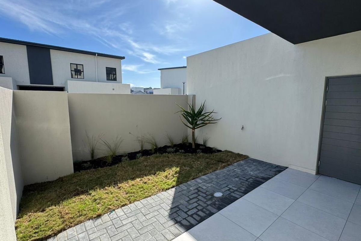 A private rear courtyard featuring a paved patio area, a small landscaped garden bed, and a secure external door.