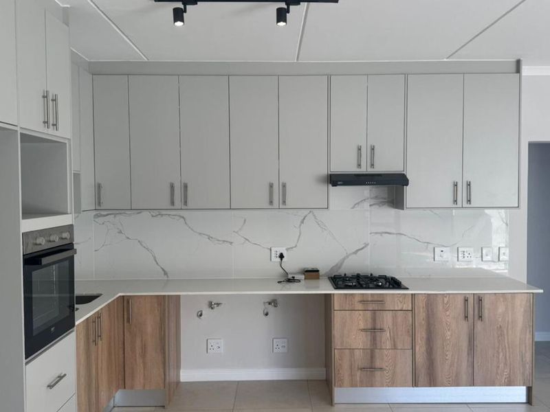 Modern kitchen featuring two-tone cabinetry, marble-look splashback, quartz countertops, built-in oven, and gas hob with an integrated extractor fan.
