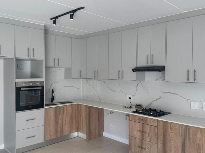 Modern kitchen featuring two-tone cabinetry, marble-look splashback, quartz countertops, built-in oven, gas hob, and integrated extractor fan.
