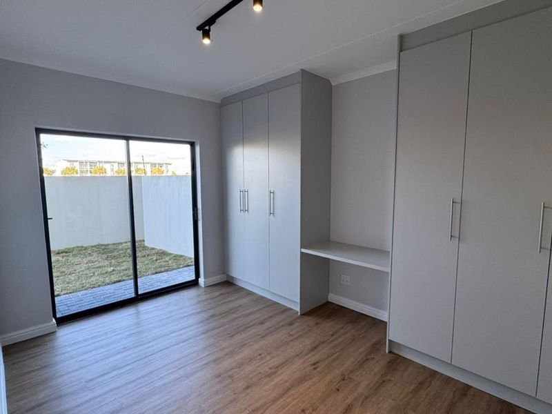 Modern bedroom featuring built-in cupboards, an integrated desk, laminate flooring, and a sliding glass door providing access to the outdoor area.