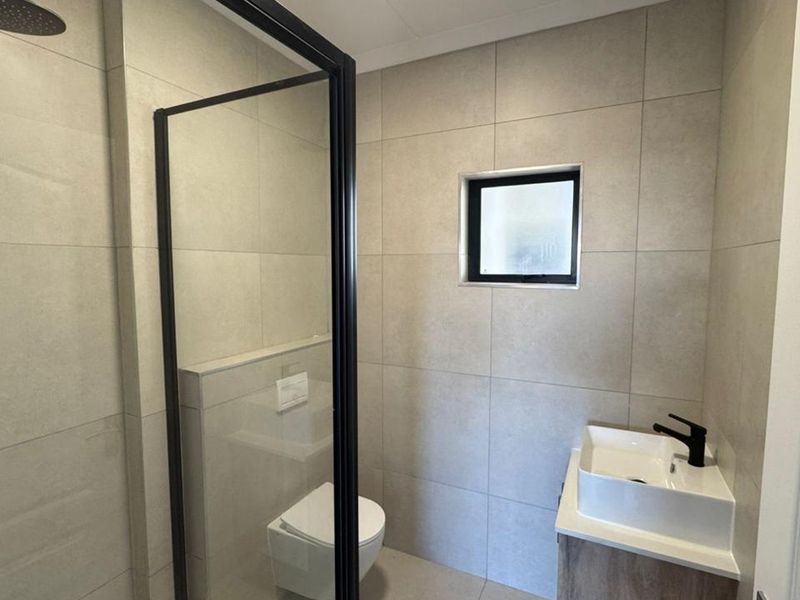 Modern bathroom featuring a walk-in shower with black-framed screen, wall-mounted toilet, and a contemporary vanity basin with black tapware.