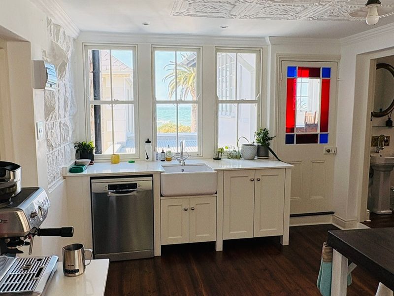 A charming kitchen featuring a farmhouse sink, integrated dishwasher, stone feature wall, and a unique stained glass door with views of the ocean.