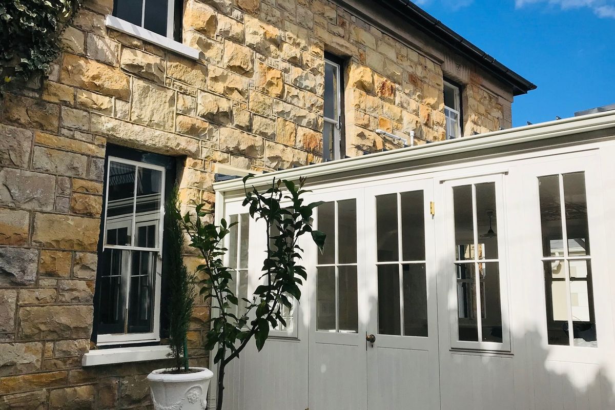 A view of the rear elevation featuring traditional stone masonry walls paired with a modern white timber-framed conservatory extension.