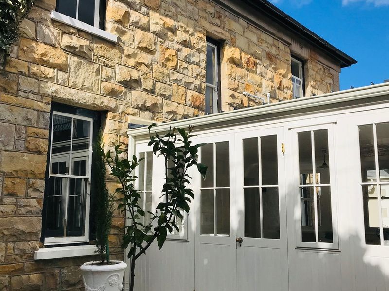 A view of the rear elevation featuring traditional stone masonry walls paired with a modern white timber-framed conservatory extension.