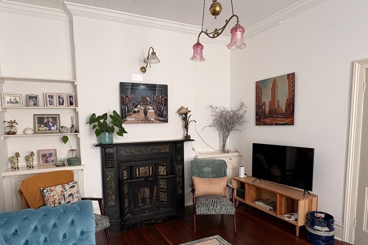 A characterful living room featuring an ornate cast iron fireplace, built-in shelving, original hardwood flooring, and classic period architectural details like coving and picture rails.