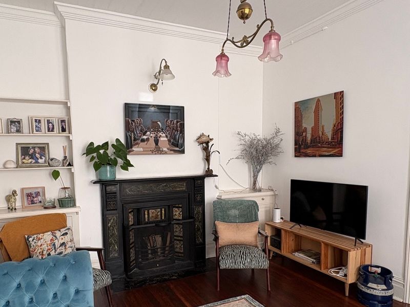 A characterful living room featuring an ornate cast iron fireplace, built-in shelving, original hardwood flooring, and classic period architectural details like coving and picture rails.