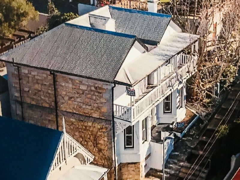 Aerial view of a two-story house featuring stone masonry walls, a corrugated metal roof, and a timber balcony.