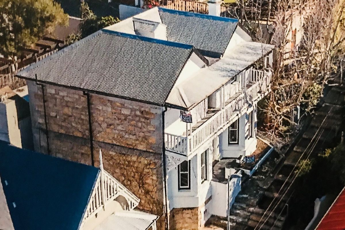 Aerial view of a two-story house featuring stone masonry walls, a corrugated metal roof, and a timber balcony.