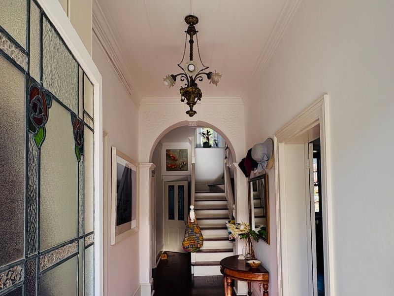 Welcoming entrance hall featuring a classic stained glass door, elegant archway, original staircase, and period architectural details including ornate ceiling molding.