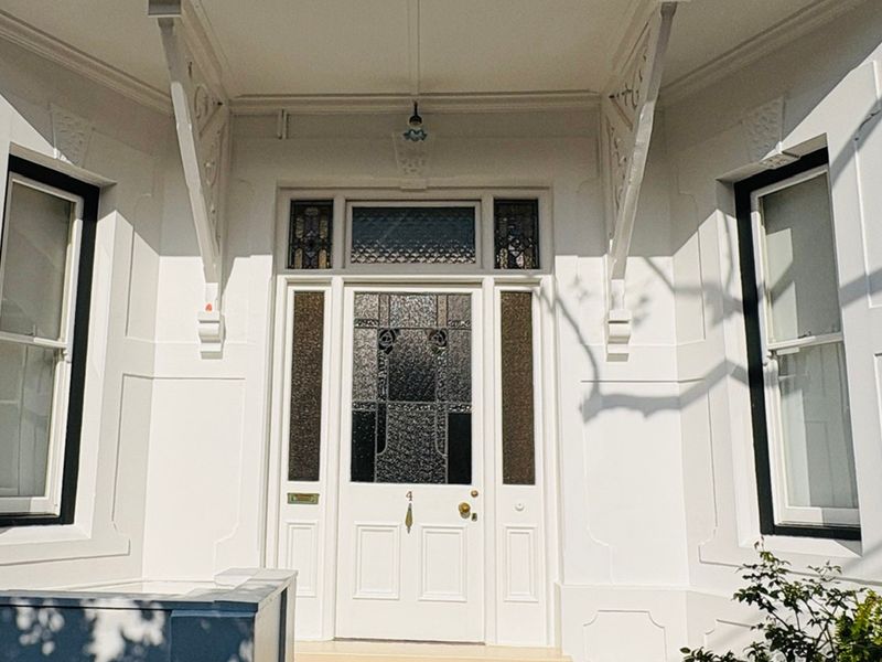 A well-maintained front entrance featuring a classic leaded glass door, decorative timber brackets, and elegant sash windows with crisp white exterior finishes.