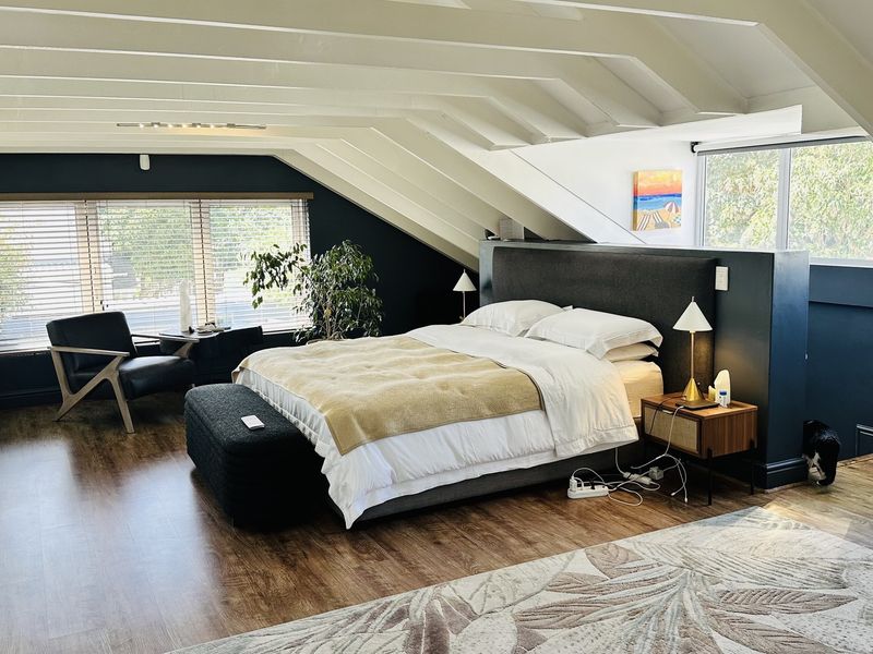 Spacious attic-style bedroom featuring exposed rafters, sloped ceilings, laminate flooring, and extensive built-in storage cabinetry.
