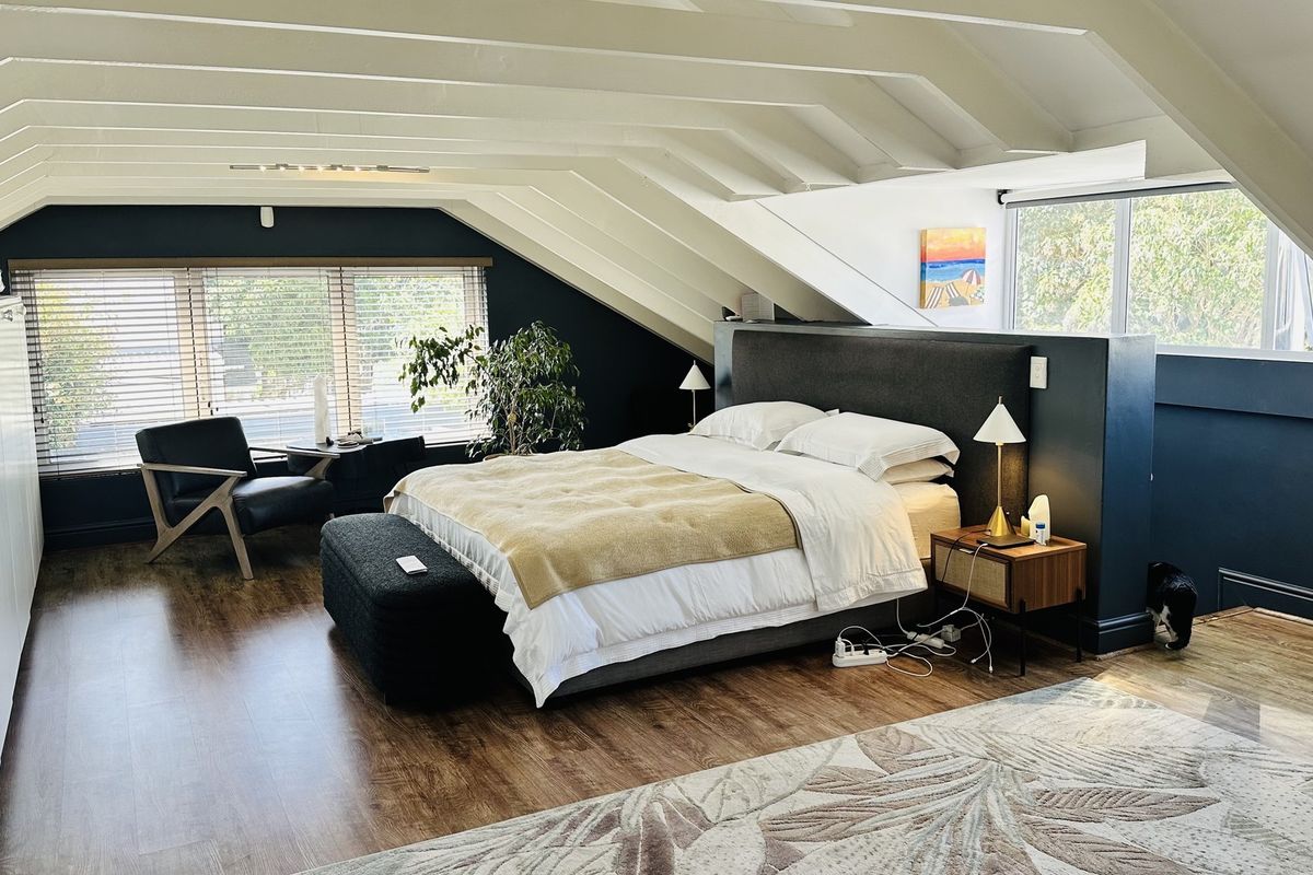Spacious attic-style bedroom featuring exposed rafters, sloped ceilings, laminate flooring, and extensive built-in storage cabinetry.