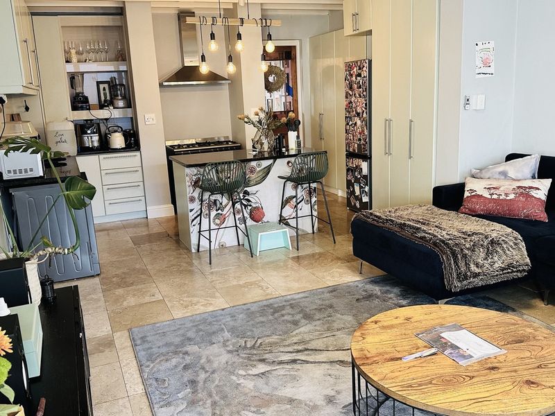 An open-plan living and kitchen area featuring stone tile flooring, a central kitchen island with a gas cooktop, and integrated cabinetry.